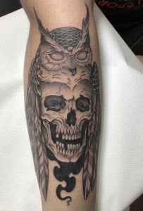 Tatuaje búho sobre calavera con plumas — CAOS Art Tattoo Chile