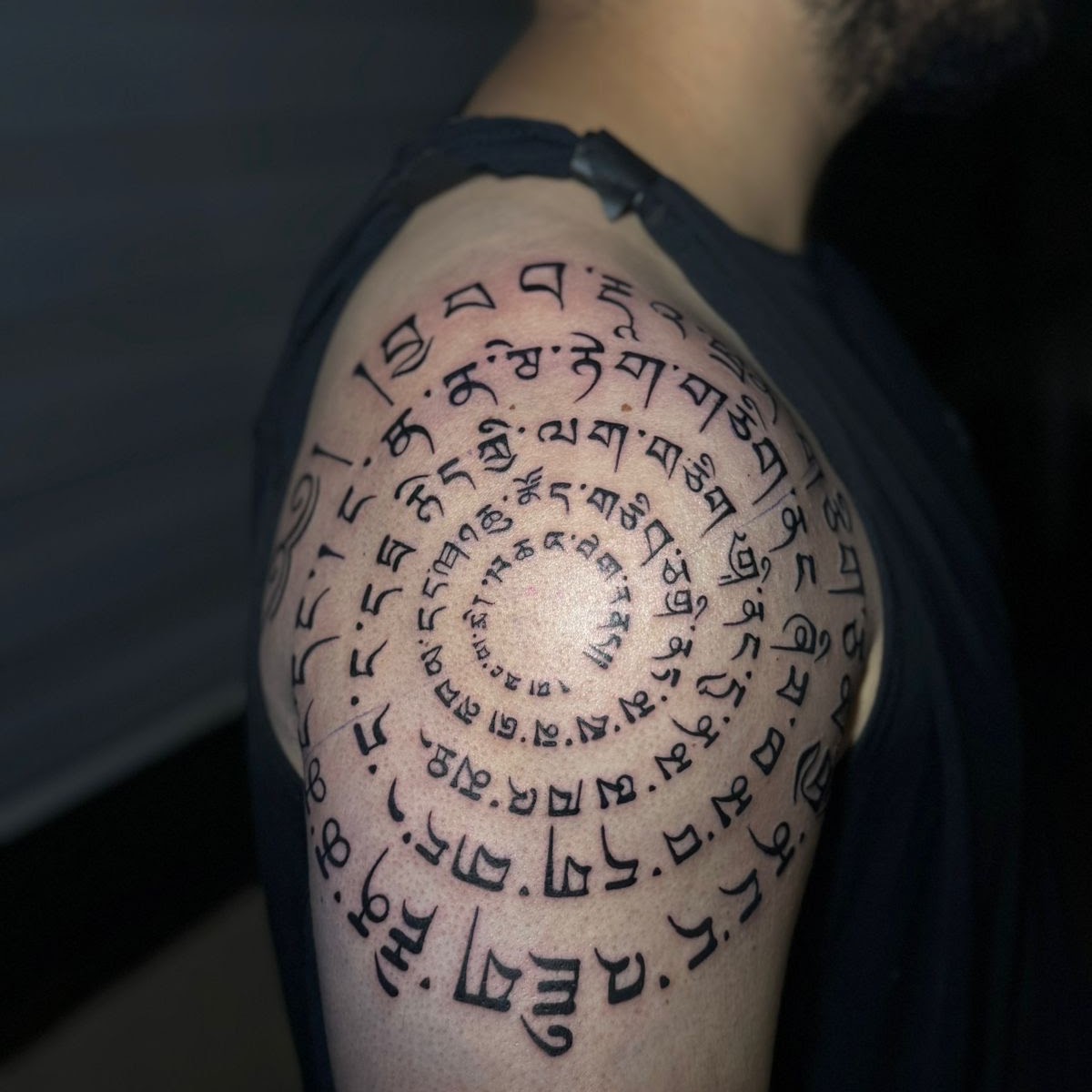 Tatuaje Mantra tibetano espiral en hombro — CAOS Art Tattoo Chile