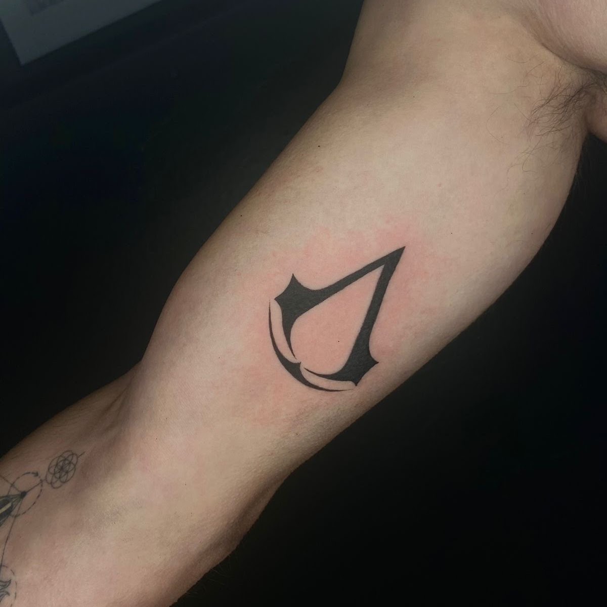 Tatuaje Logo Assassin's Creed blackwork sólido — CAOS Art Tattoo Chile